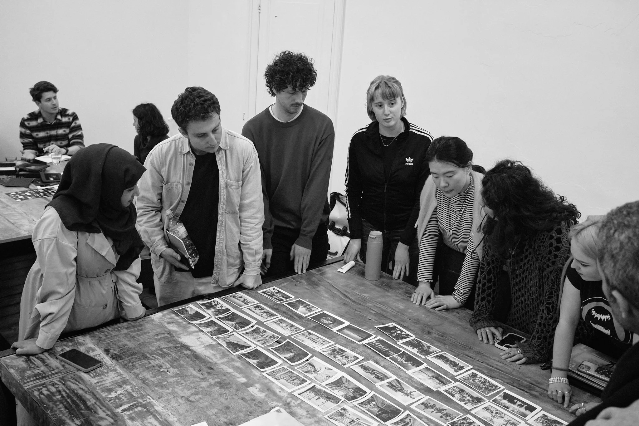 A group of makers gathered around a table, attentively viewing a sequence of photographs spread out for feedback.