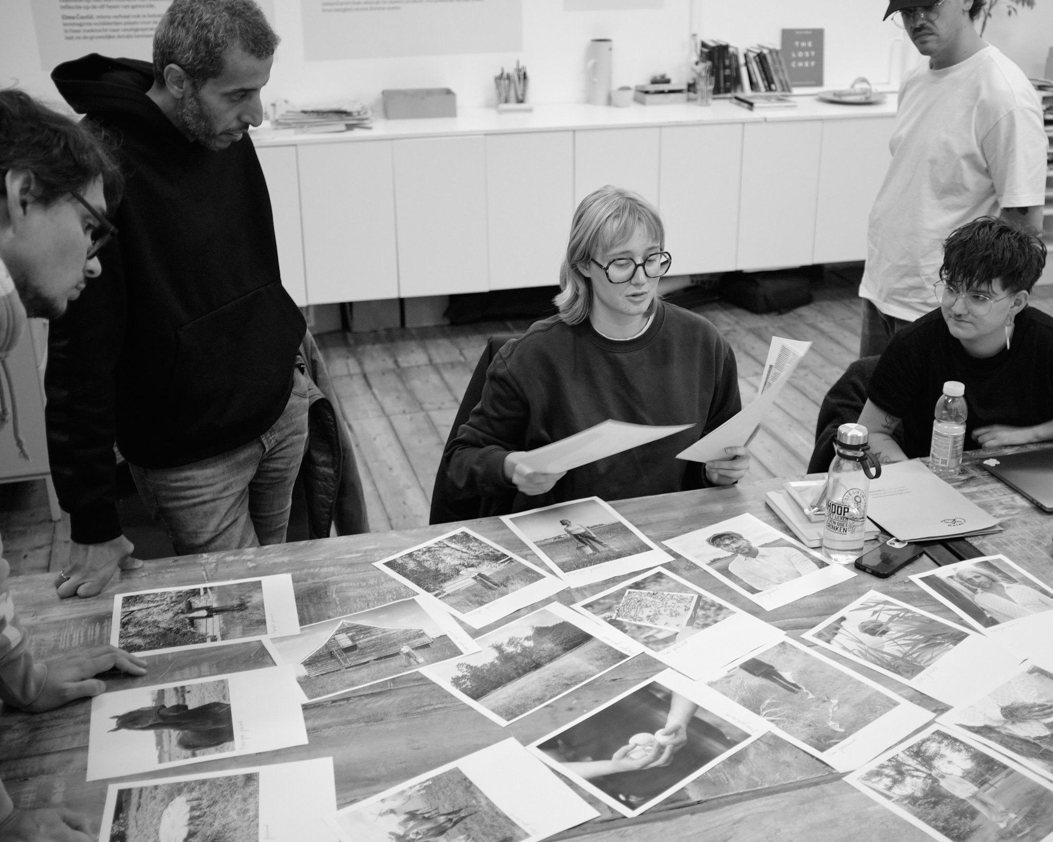 A photographer presents prints laid out across a table while peers look on during a Wanderstories feedback round.