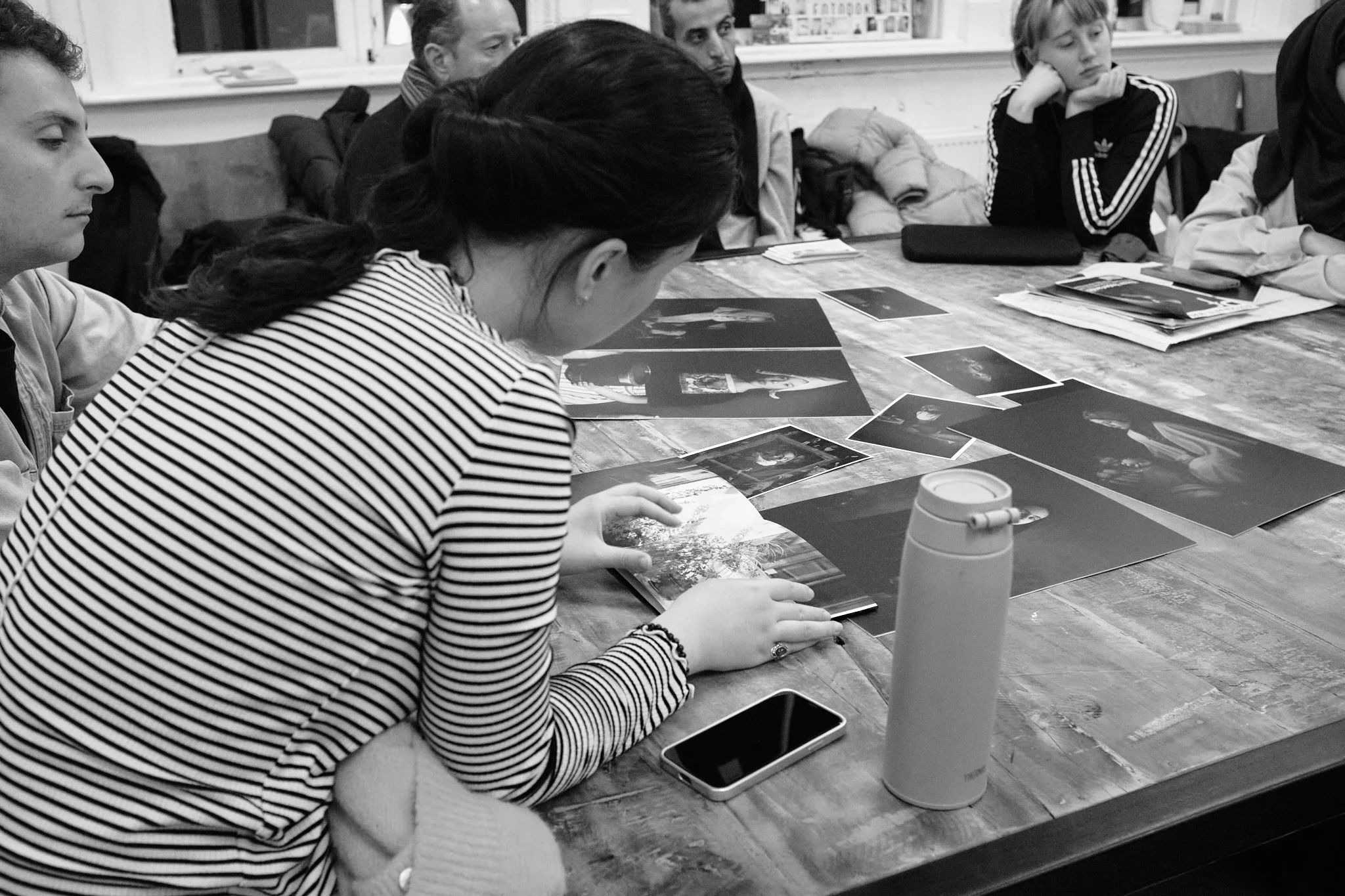 A participant leans over a table to look closely at a row of portrait prints while others watch during a Wanderstories session.