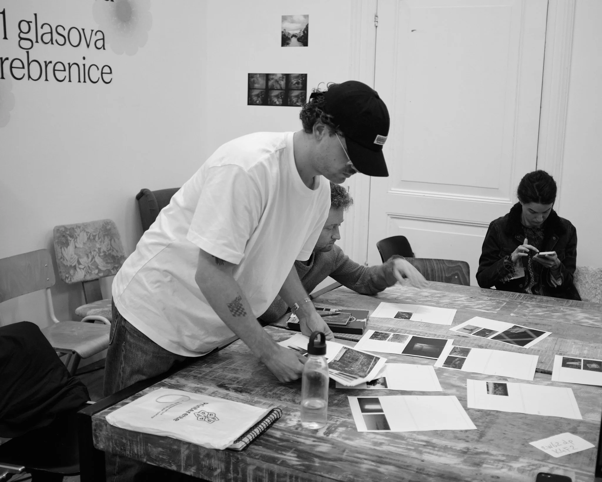 A photographer leans over the table to arrange his prints during a Wanderstories session, while another participant looks on and a third checks her phone in the background.