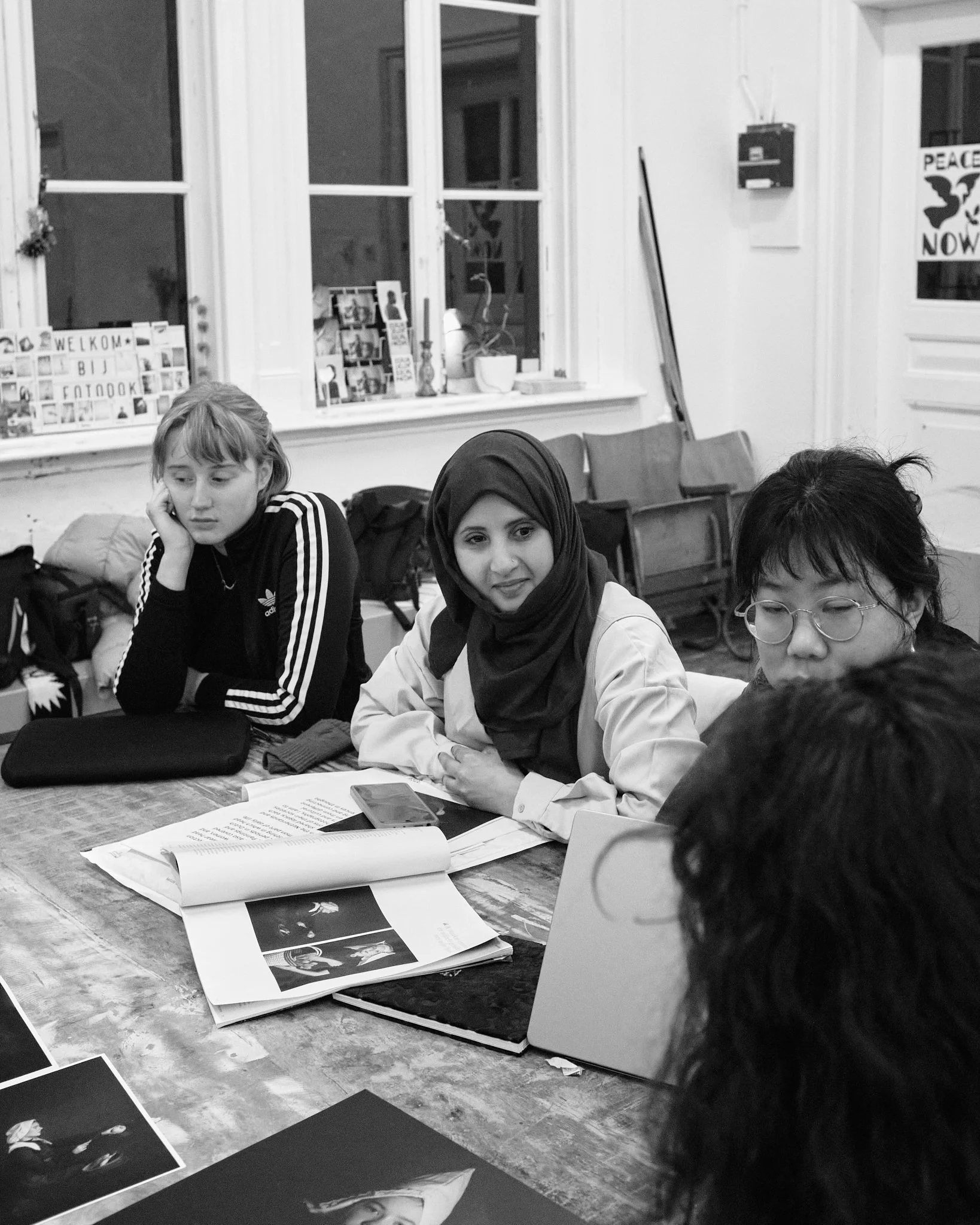 Three participants seated at a table at Fotodok, looking at an open photobook during a feedback session.