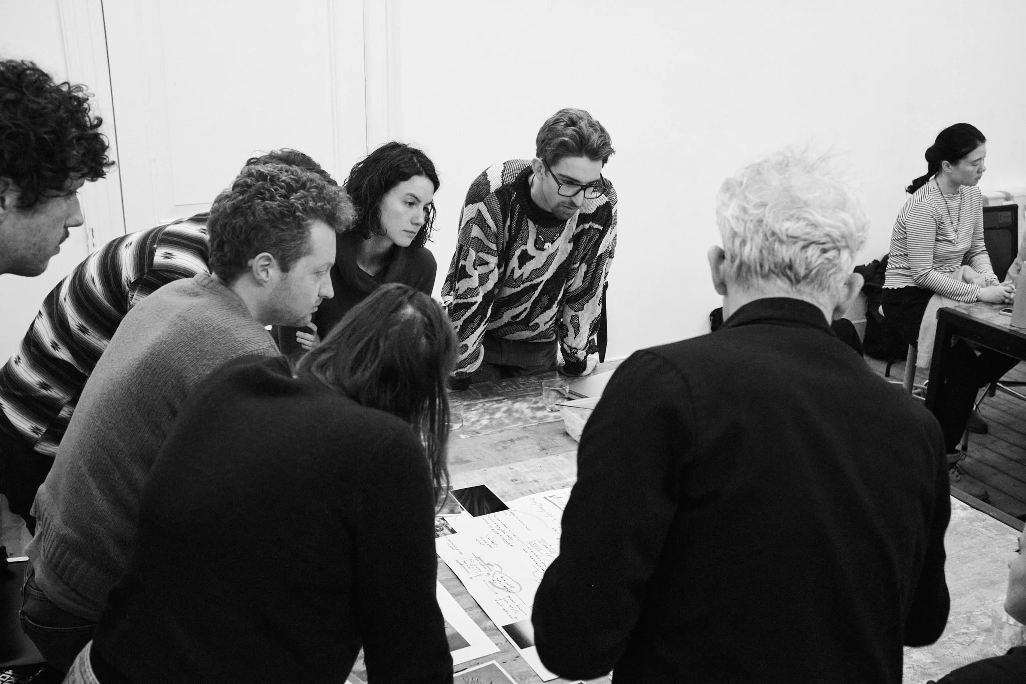 A group of makers leaning over a table, closely studying printed photographs and notes during a feedback session.