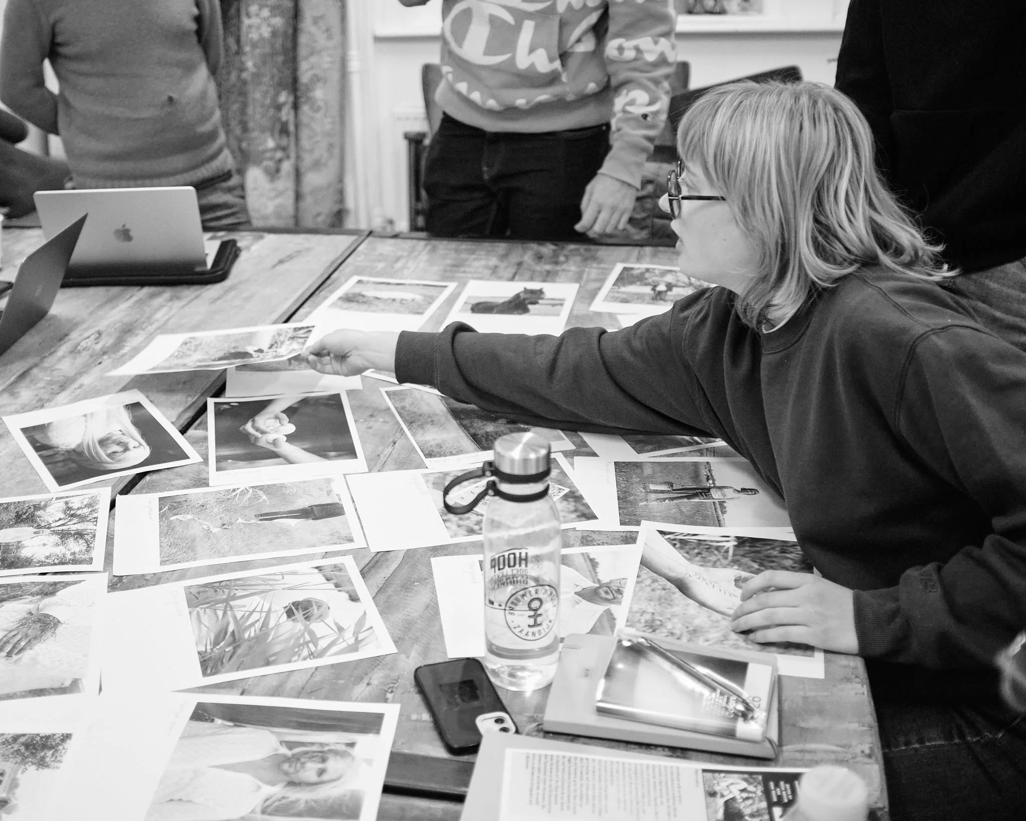 A participant reaches across a table covered with photographic prints, pointing to an image during a Wanderstories discussion.