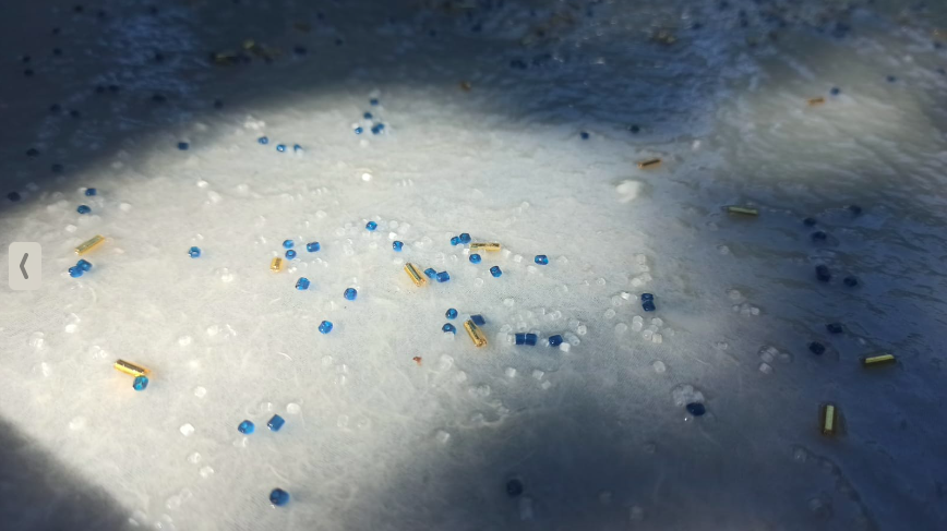 Close-up view of a white frosting surface decorated with small blue and white sprinkles, along with tiny gold-colored cylindrical sprinkles.