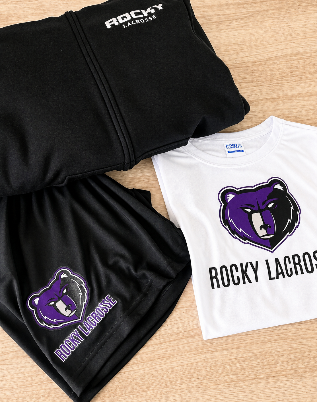 Black hoodie and black shorts with Rocky Lacrosse logos, and a white T-shirt with a purple and black bear logo and Rocky Lacrosse written underneath.