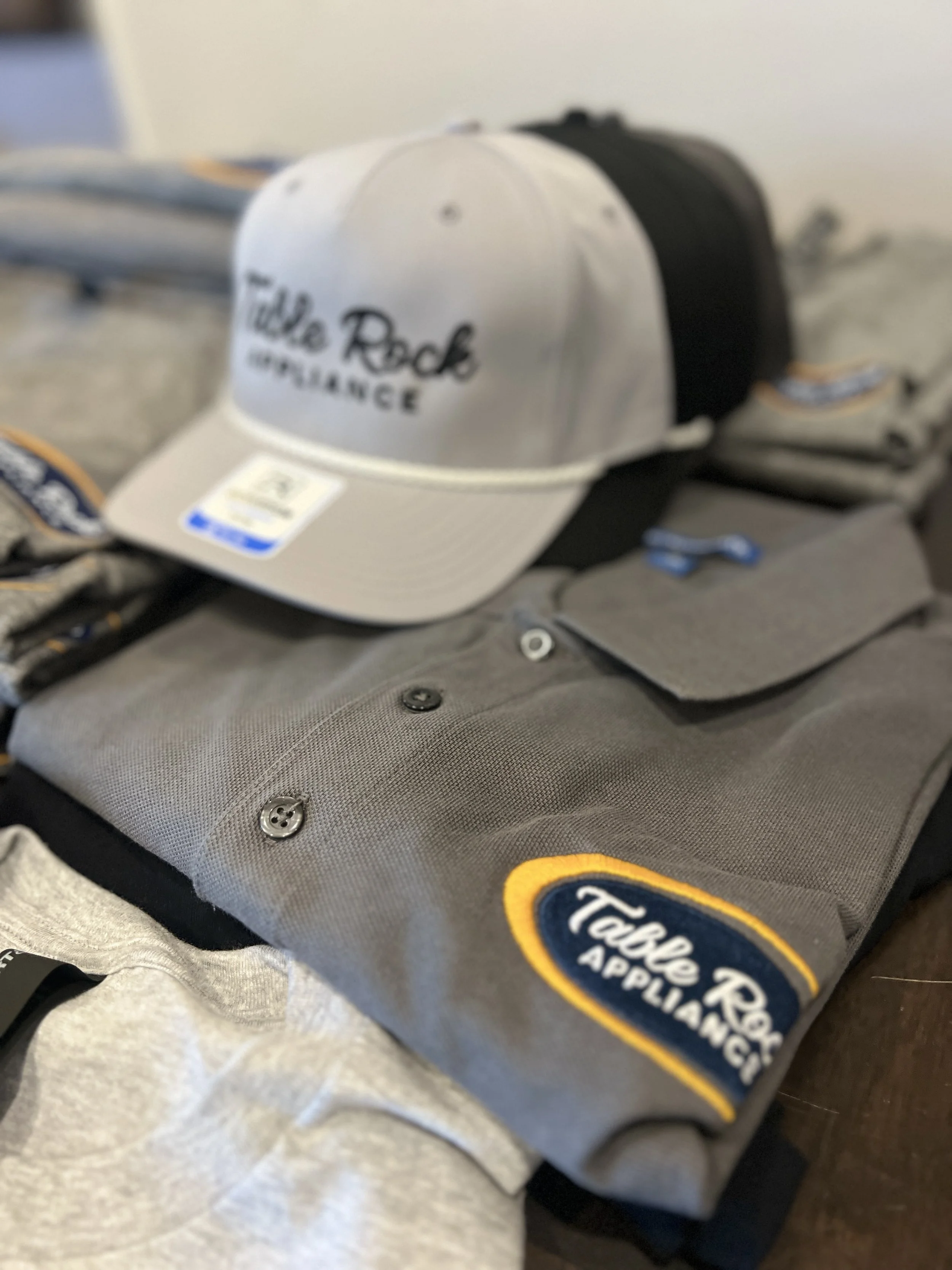 A gray fabric bag with a yellow and blue patch that reads "Tackle Reapplications" and a white cap with black text that says "Tackle Reapplications" resting on top of the bag.