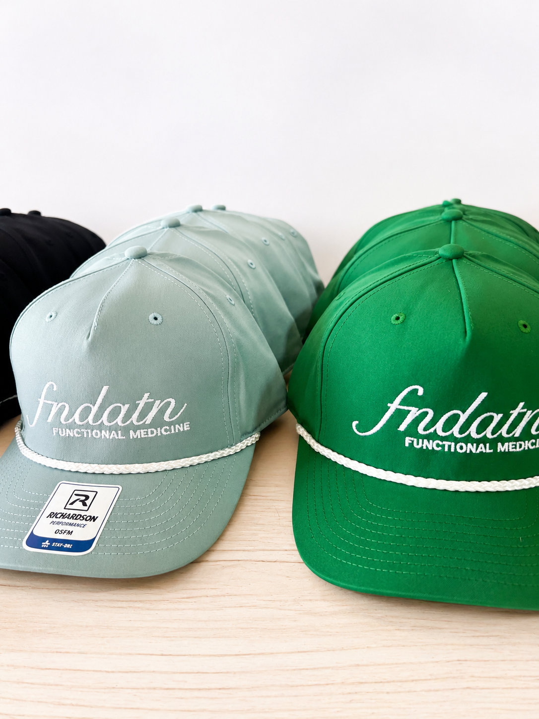 Several baseball caps with 'fndatrn FUNCTIONAL MEDICINE' embroidered on the front, displayed on a light wooden surface.