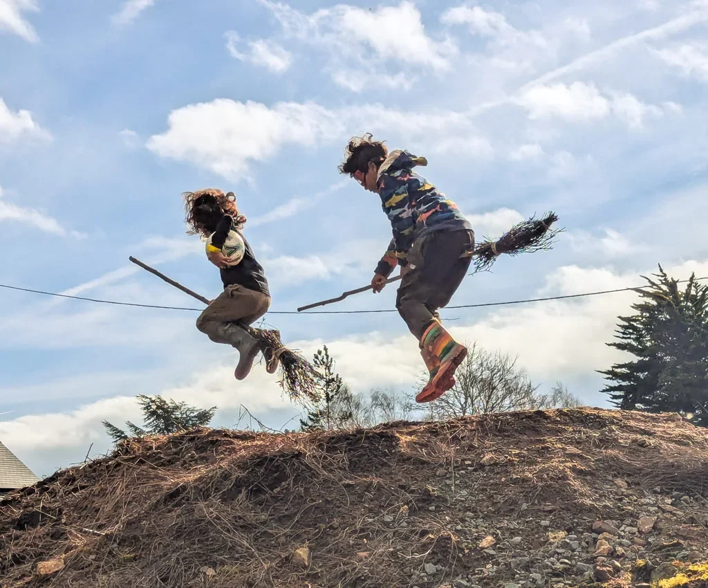 Children on a hilltop pretending to fly on brooms at Eyton Burrow
