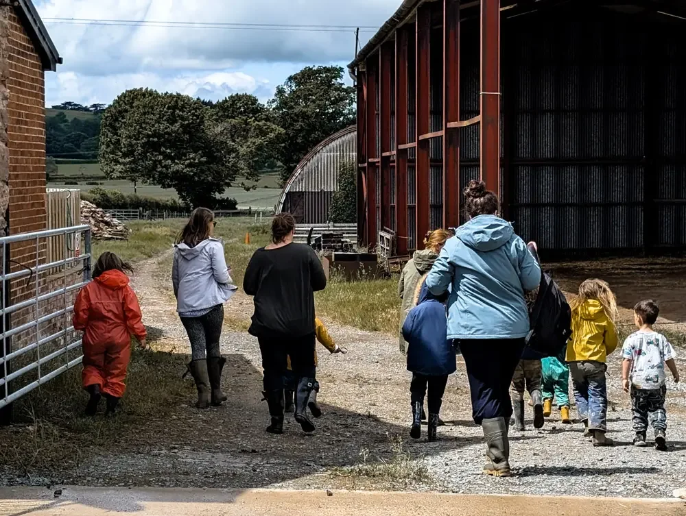 Children and adults walking down a farm track past red barns at Eyton Burrow