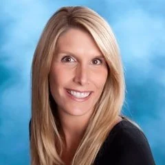 Portrait of a woman with long blonde hair, smiling, against a blue background.