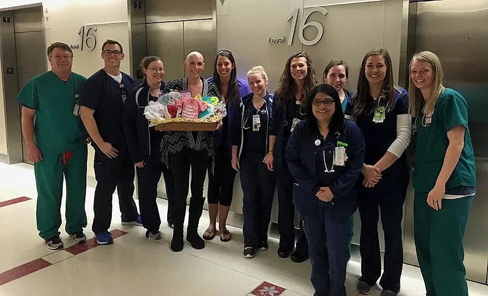 Group of healthcare professionals, some in scrubs, standing in a hospital hallway, with one woman holding a basket of gifts.