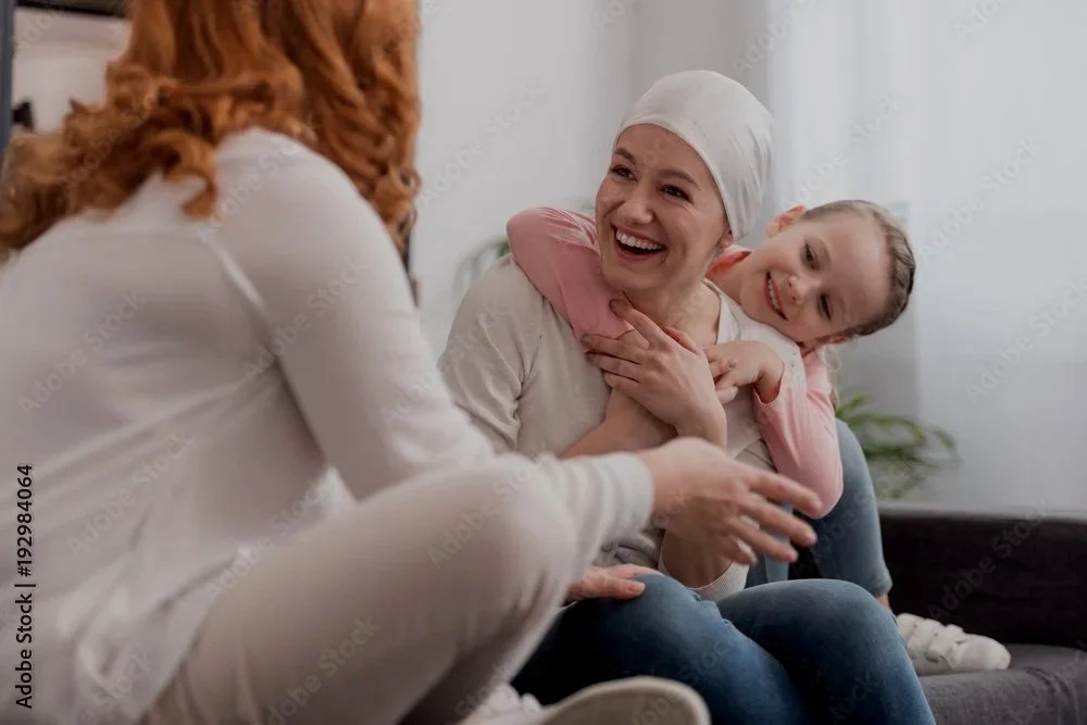 A woman with a headscarf and a young girl are happily talking to a red-haired woman with curly hair, all sitting on a couch.