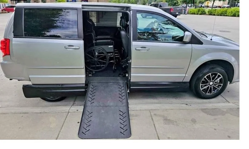 Silver van with a wheelchair accessible ramp extended from the side door, parked in an outdoor lot.