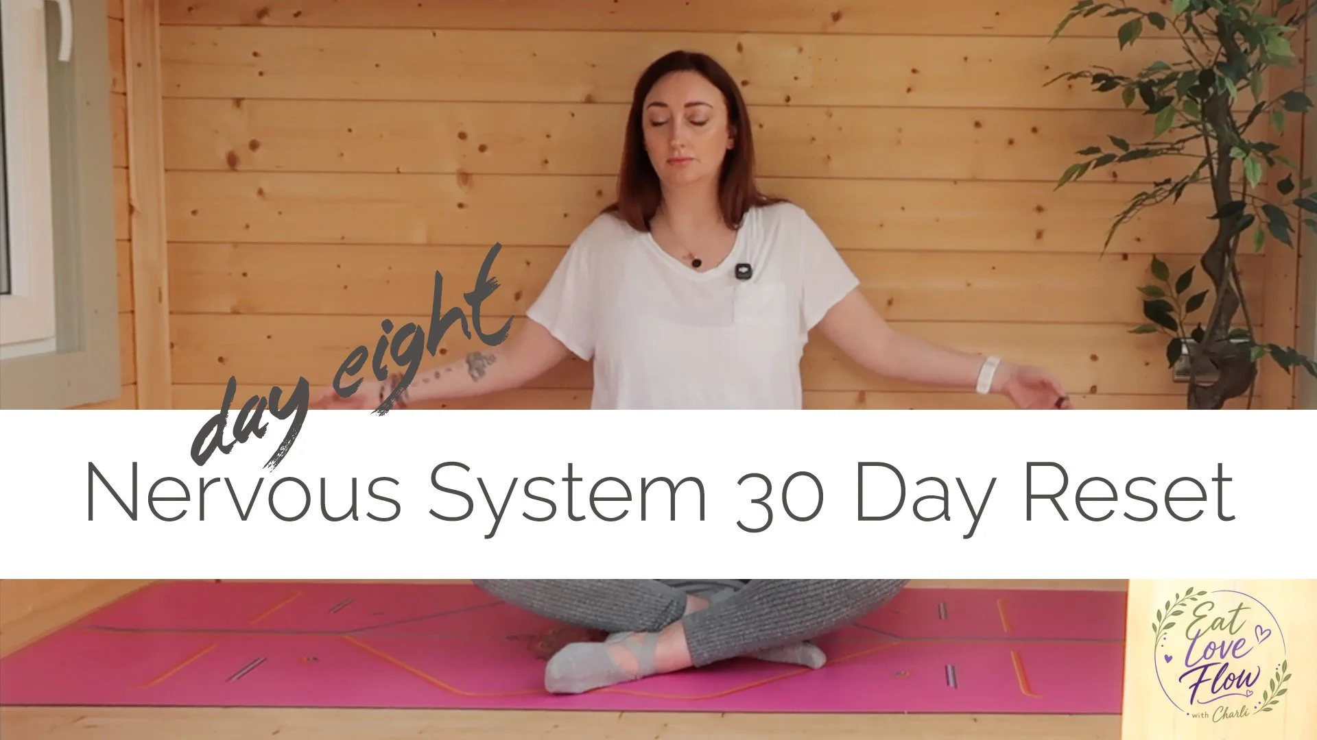 A woman sitting cross-legged on a yoga mat with a wooden wall behind her. She has her eyes closed and arms extended outward. Text overlay says 'day eight' and 'Nervous System 30 Day Reset.'