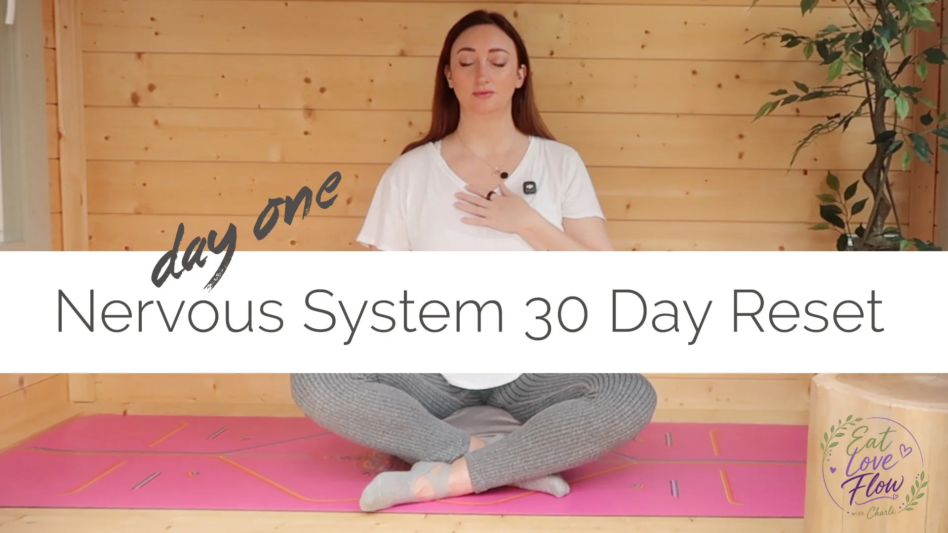 A woman sitting cross-legged on a yoga mat, practicing meditation with her eyes closed, in a wooden room with a large potted plant, promoting a 30-day nervous system reset.