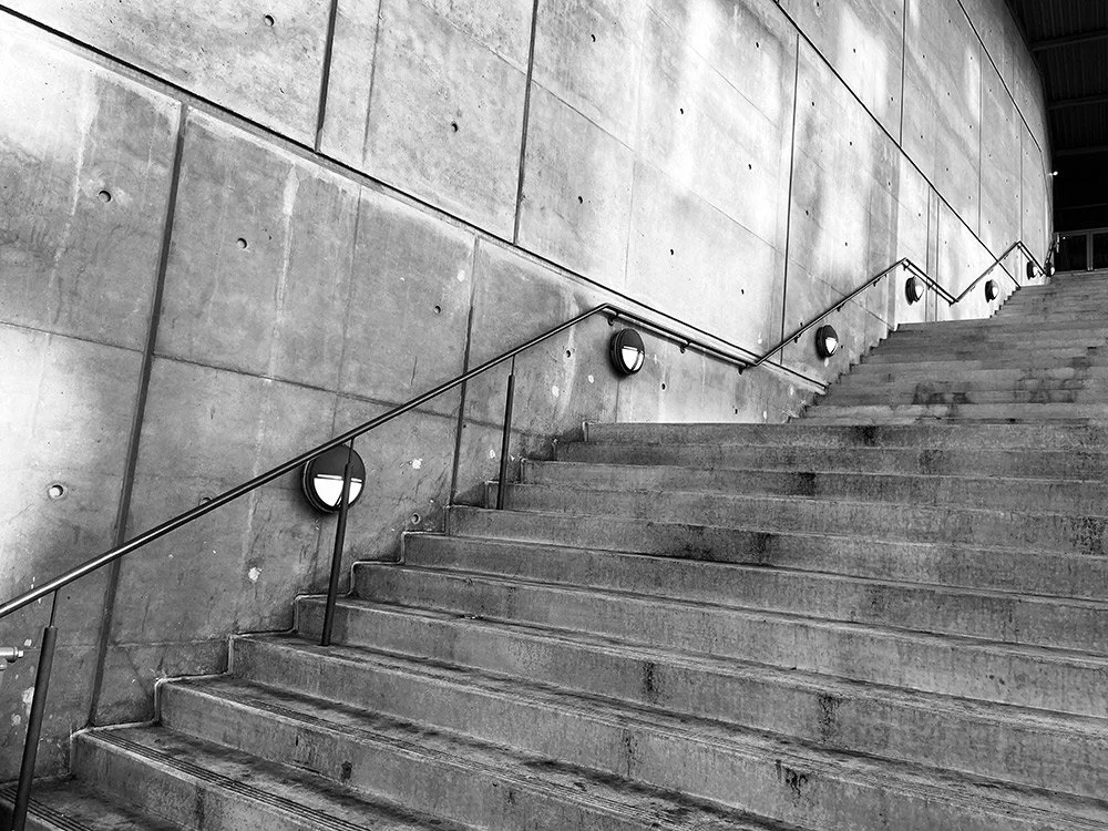 Concrete stairway with metal handrail and round wall-mounted lights along a modern concrete building exterior.