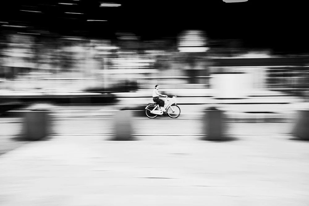 Person riding a bicycle on a street with motion blur in a cityscape.