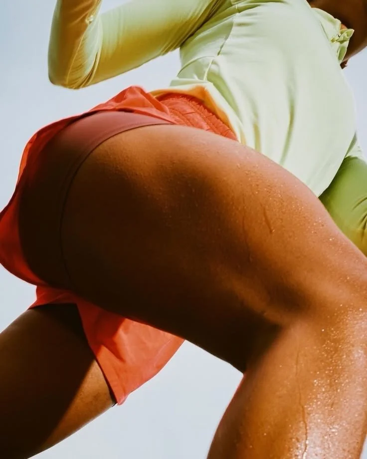 Une personne en tenue de sport, de dos, sous un éclairage natural, portant un short orange et un haut jaune clair.