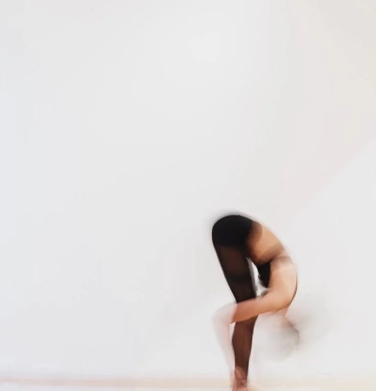 Une femme s'étire dans une pièce blanche, en position accroupie, portant un haut noir et une jupe blanche.