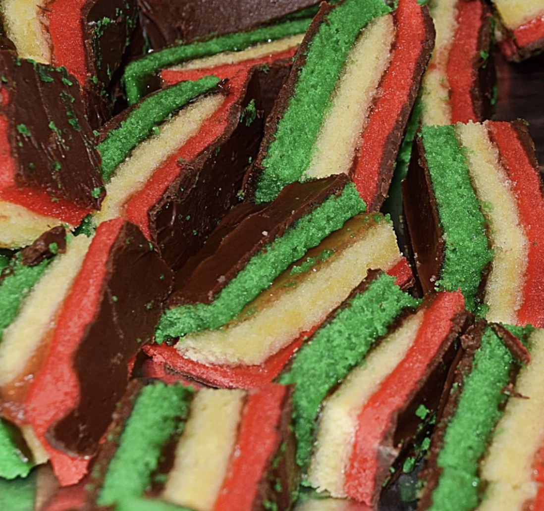 Close-up of striped layered Christmas cookies with red, white, and green colors, coated with chocolate and sprinkles available as a dessert option from Holy Roses Pizza in the Hamptons.