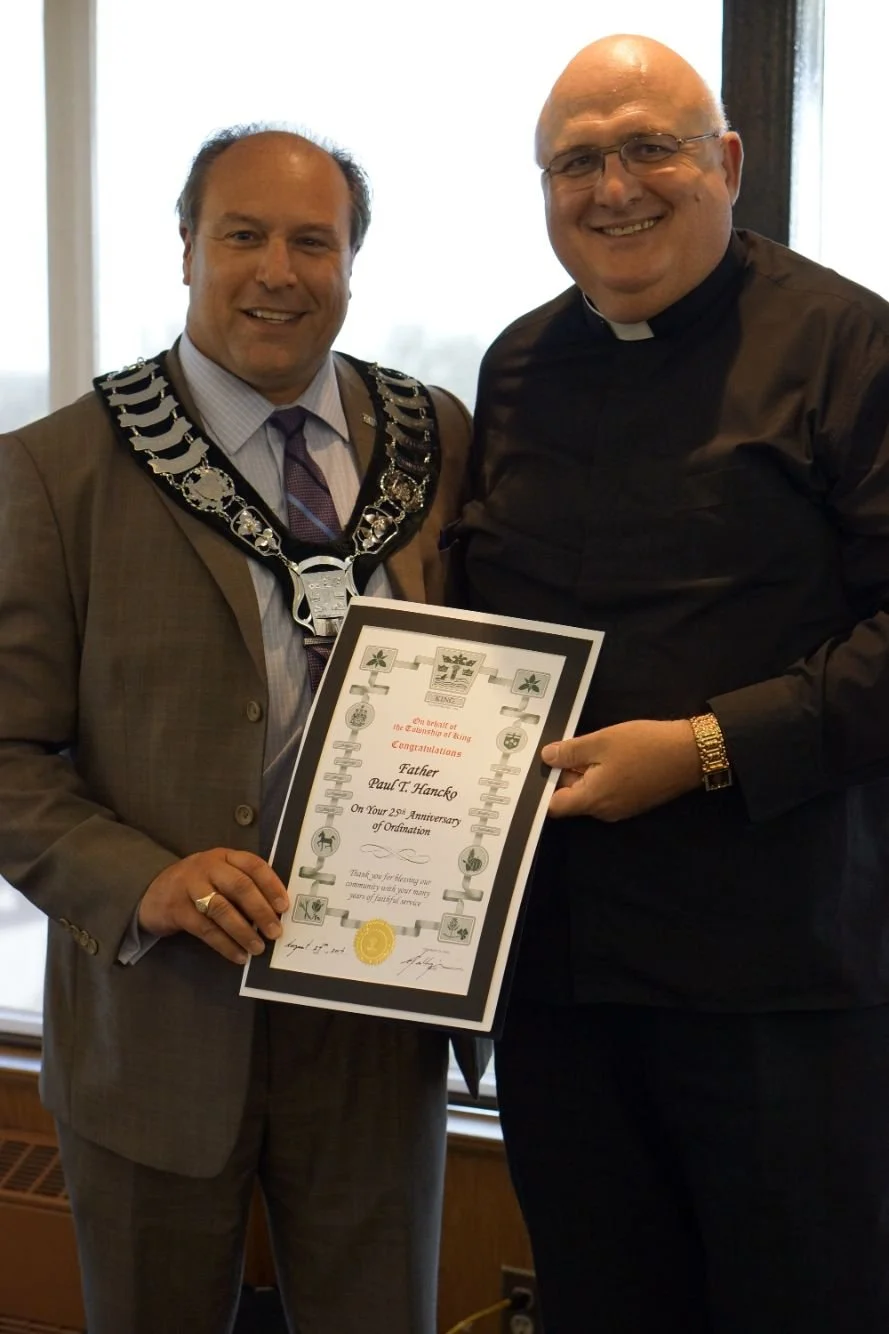 Mayor Steve Pellegrini, holding a framed certificate celebrating a 25th anniversary of ordination.