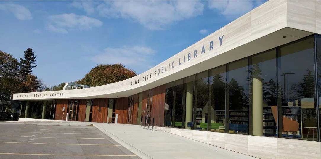 Award winning King City Public Library building with large glass windows and parking lot in front.