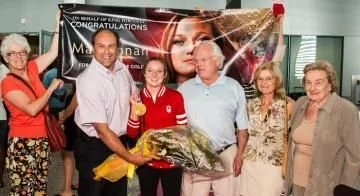 Group of six people celebrating an achievement indoors, with a banner in the background and one person holding a bouquet of flowers.