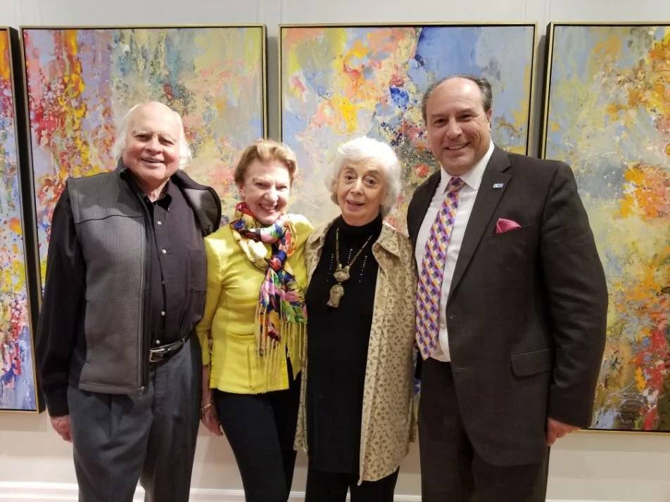 Four people standing together at an art gallery with colorful abstract paintings in the background.