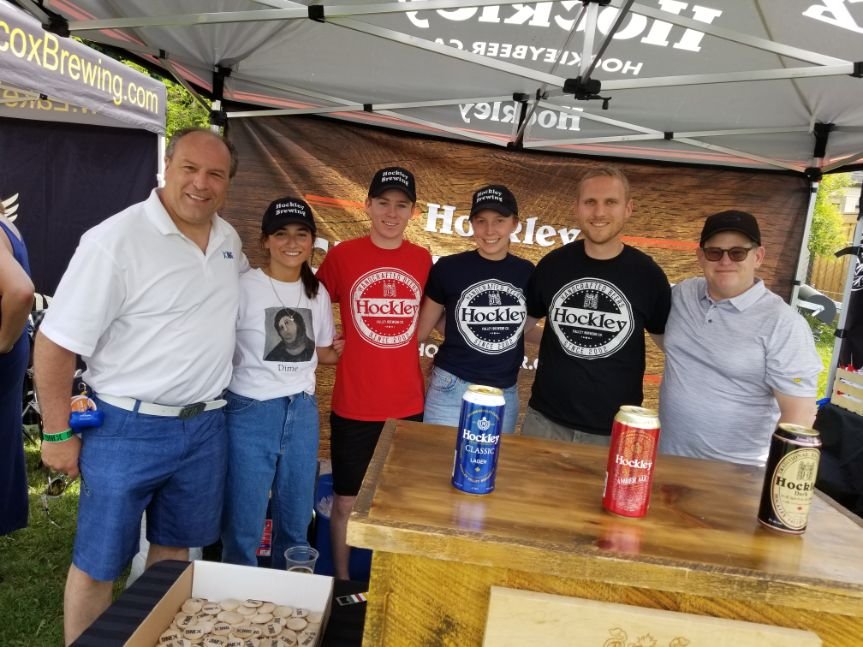 	
Mayor Steve Pellegrini standing behind a wooden table with tall cans of Hockley beer at an outdoor event, under a tent with Hockley branding.