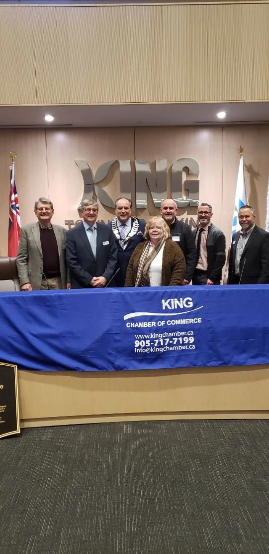 Steve Pellegrini standing behind a blue tablecloth with the logo and contact information of the King Chamber of Commerce, in front of a wall with the King's logo and flags.