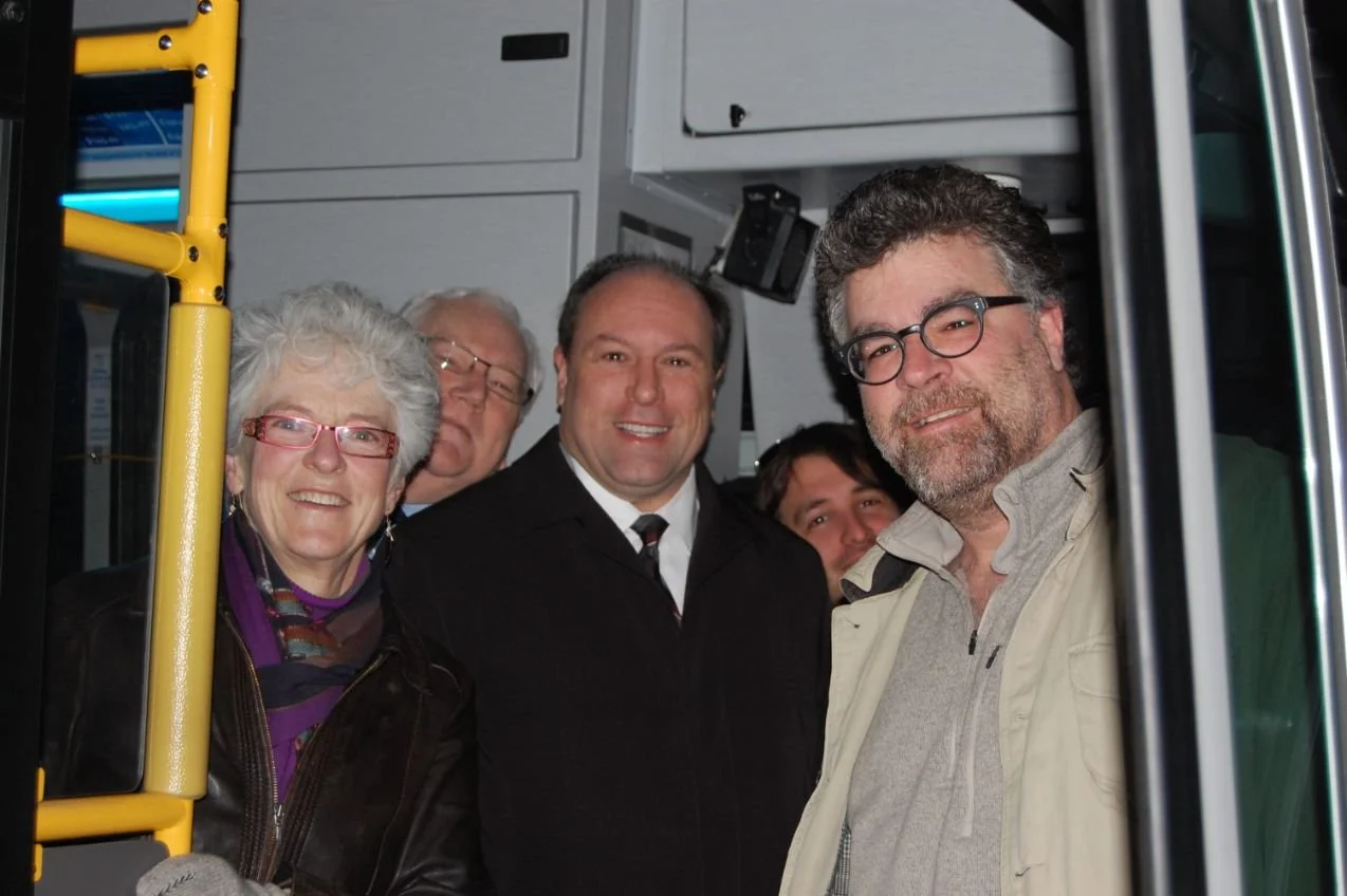 Steve Pellegrini smiling, standing inside a bus or train, with some yellow handrails visible on the left.
