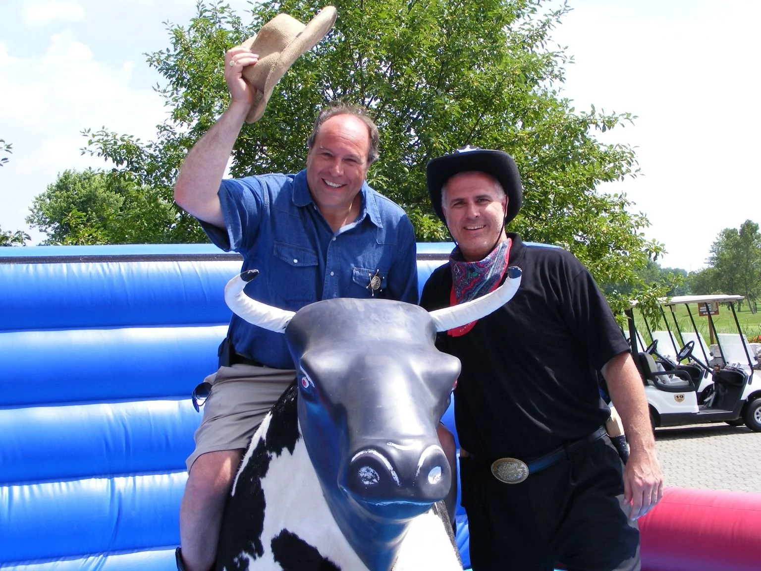 Two men dressed as a sheriff and a cowboy posing with a decorated cow statue at an outdoor event.