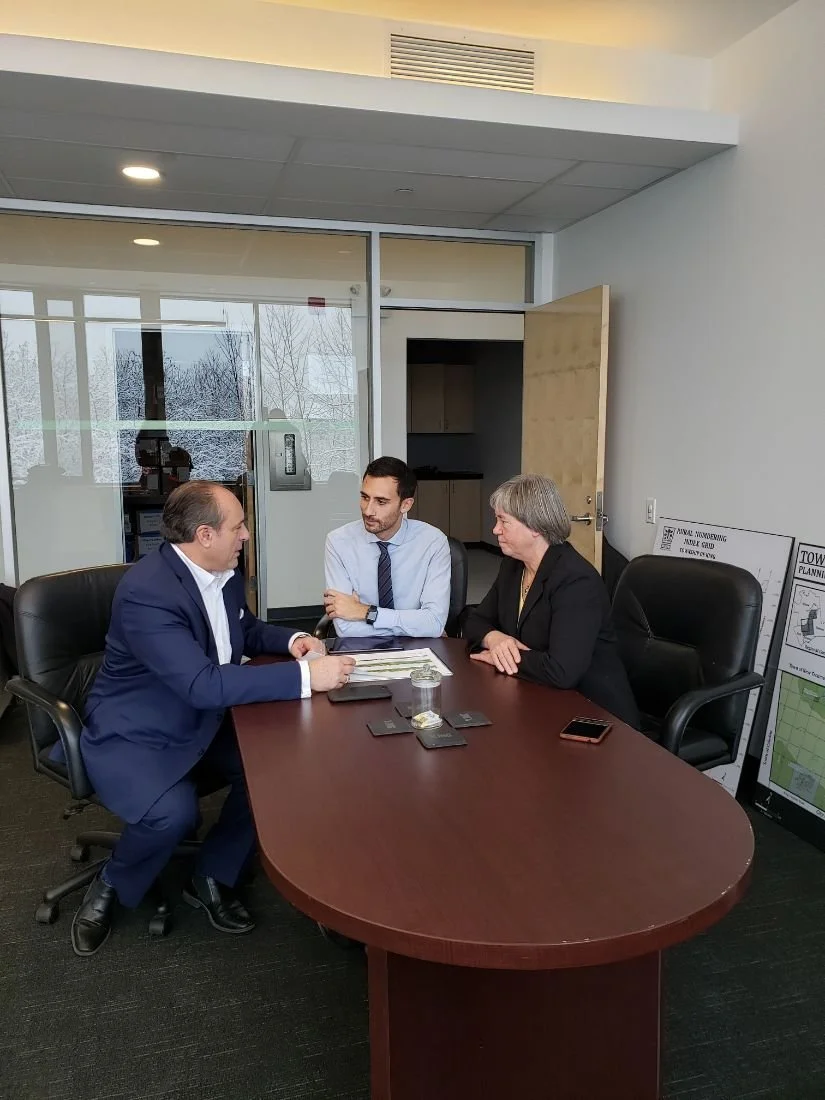 Three people seated at a conference table engaged in a discussion in a modern office setting.