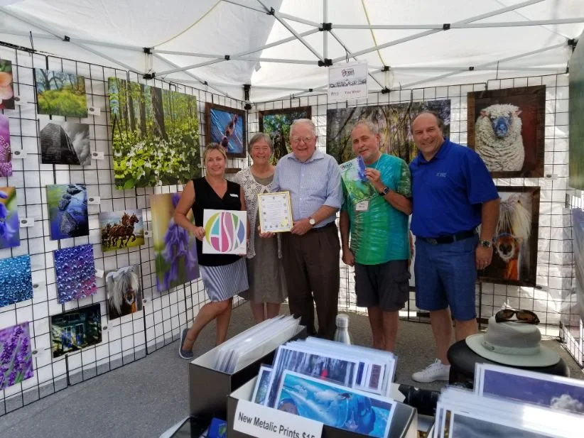 Group of five people inside an art booth with animal and nature photographs displayed on a grid wall.
