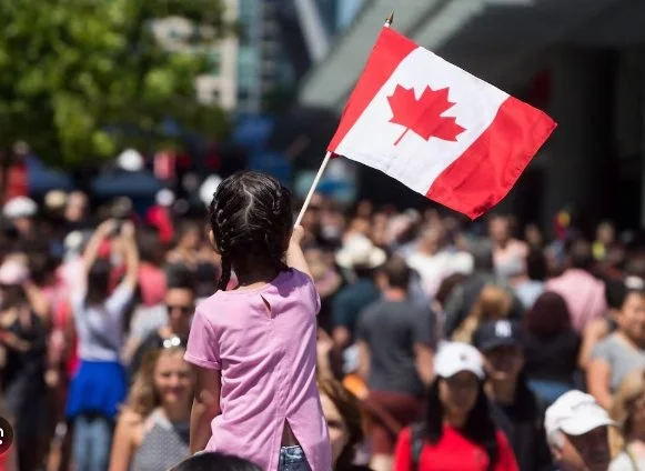 A young girl with braided hair holding a Canadian flag at a crowded outdoor event.