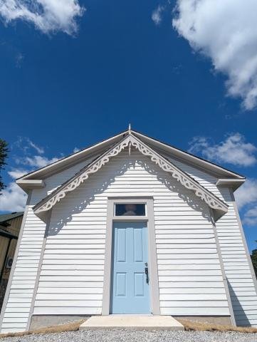 A heritage church with a white cross and the sign 'King Bible Church' on it, surrounded by green grass and trees, under a blue sky with some clouds.