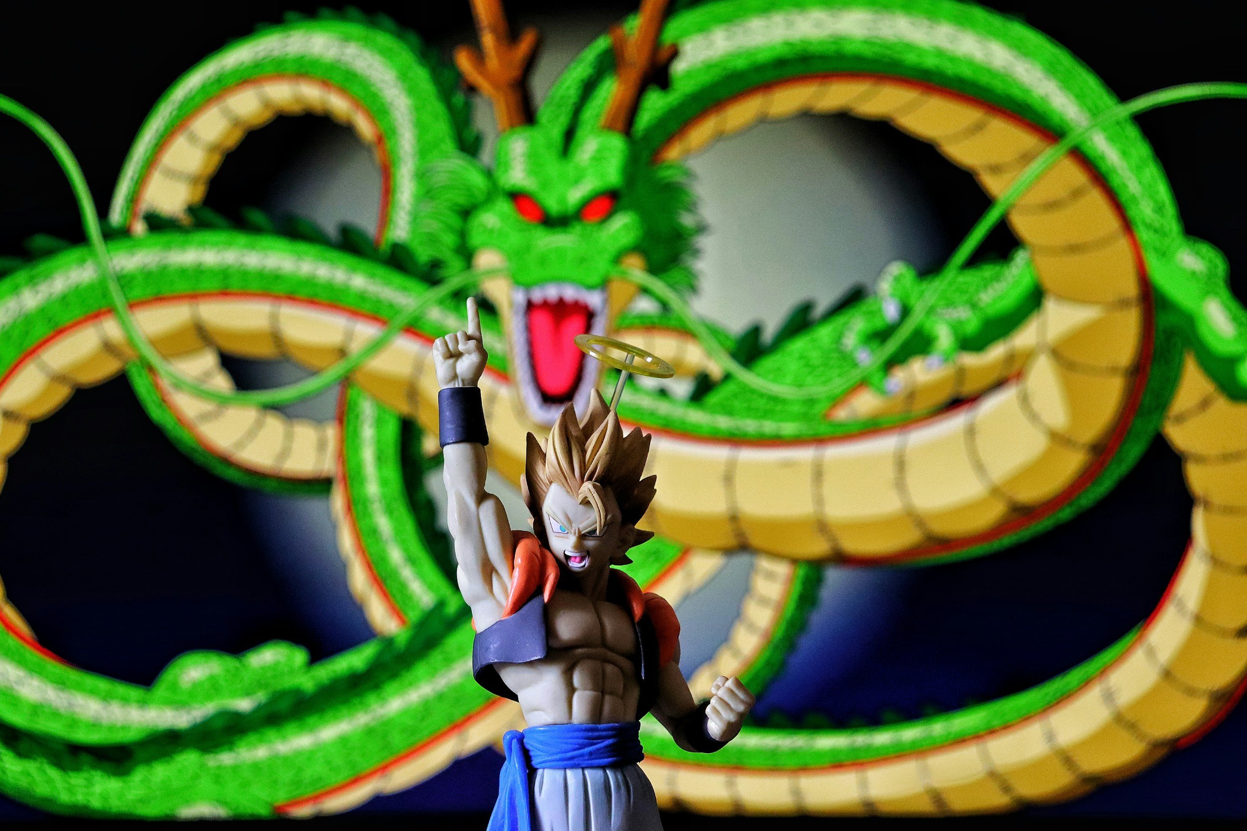 A figurine of a muscular anime character with spiky hair, raising one fist, in front of an illuminated, large green and yellow dragon lantern with red eyes and an open mouth.