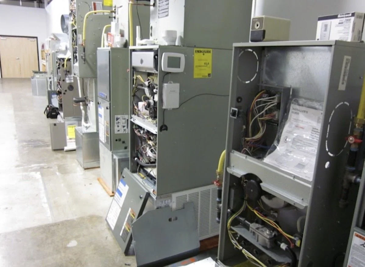 Line of HVAC or electrical equipment units with open panels, wires, and components in a warehouse or utility room.