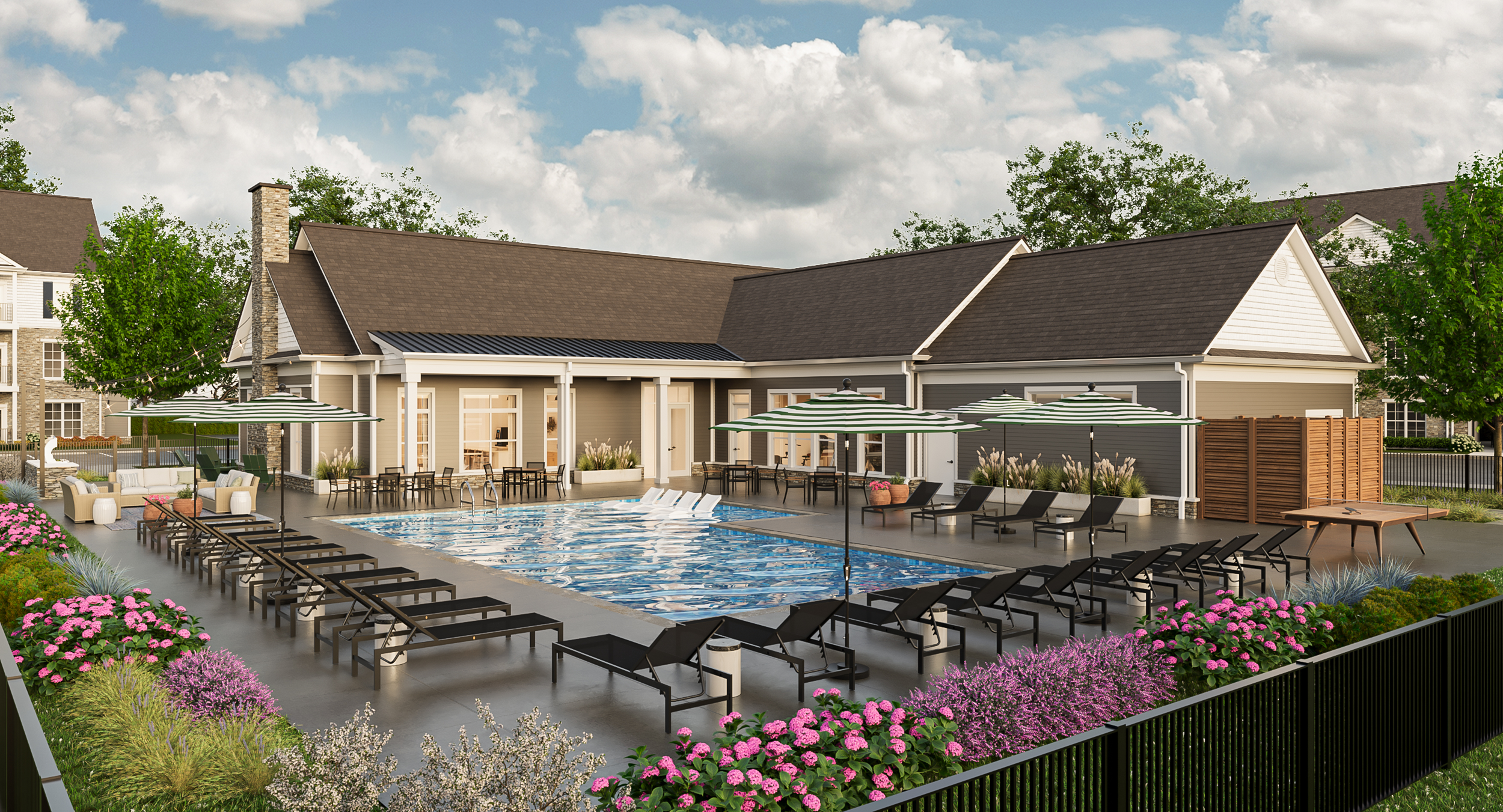 A tranquil outdoor swimming pool area with lounge chairs, umbrellas, and seating, surrounded by colorful flowers and greenery, adjacent to a house with a patio and garden.