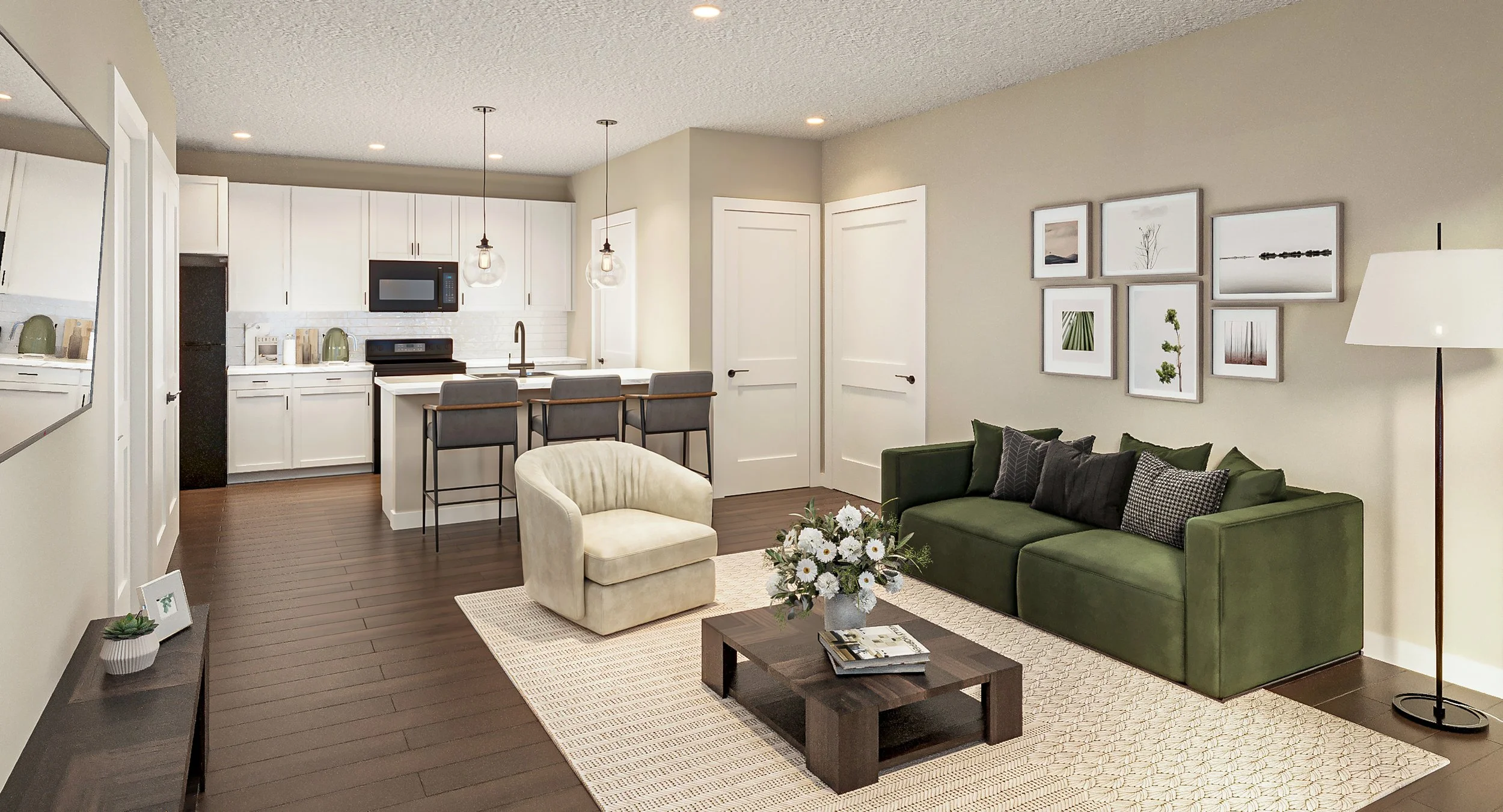 Open-concept one-bedroom living room and kitchen with a green sofa, beige armchair, and a wooden coffee table with a flower arrangement, white walls with framed art, and a dark wood floor.