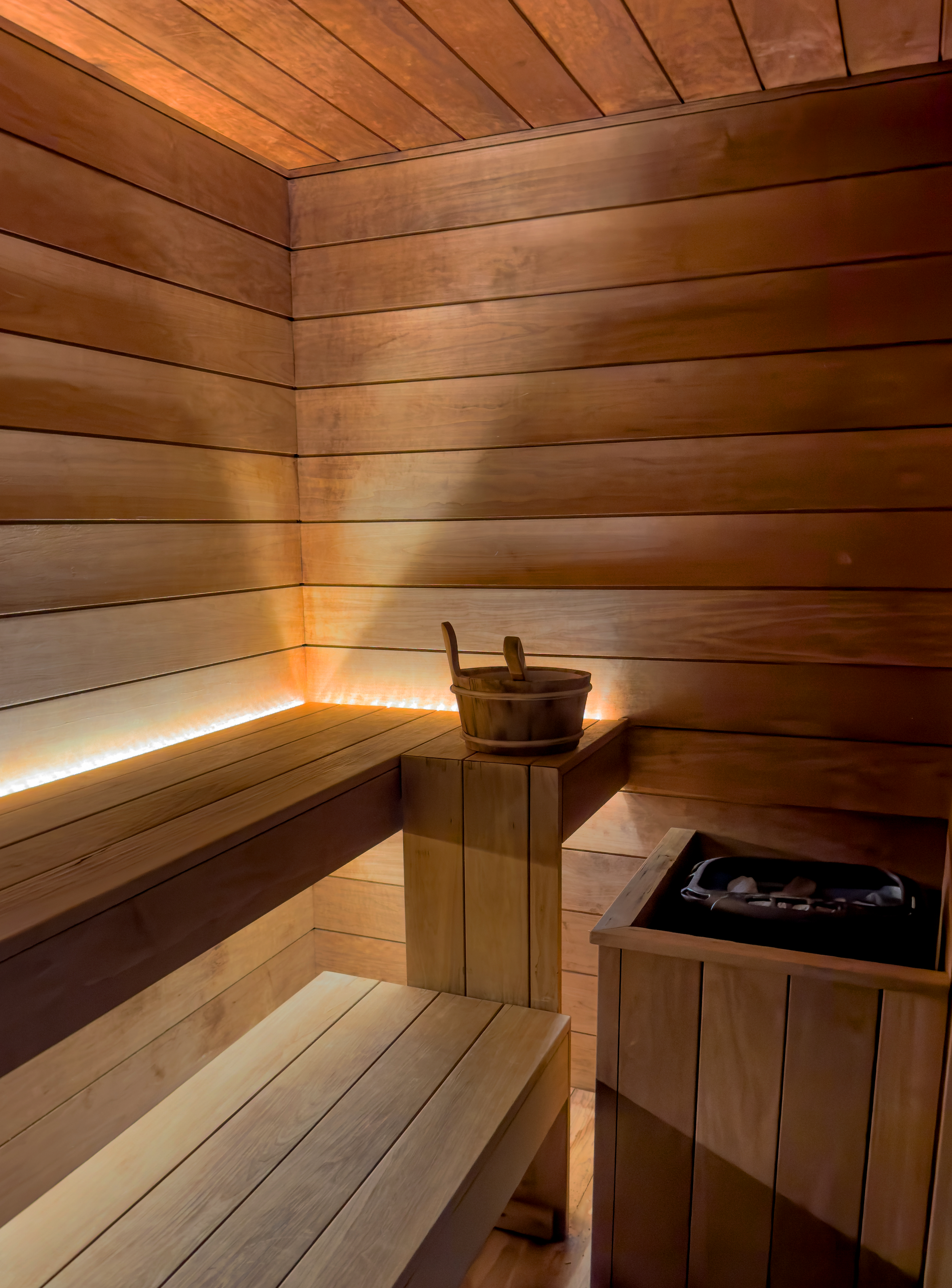 A wooden sauna room with seating, a bucket, and a heater with stones.