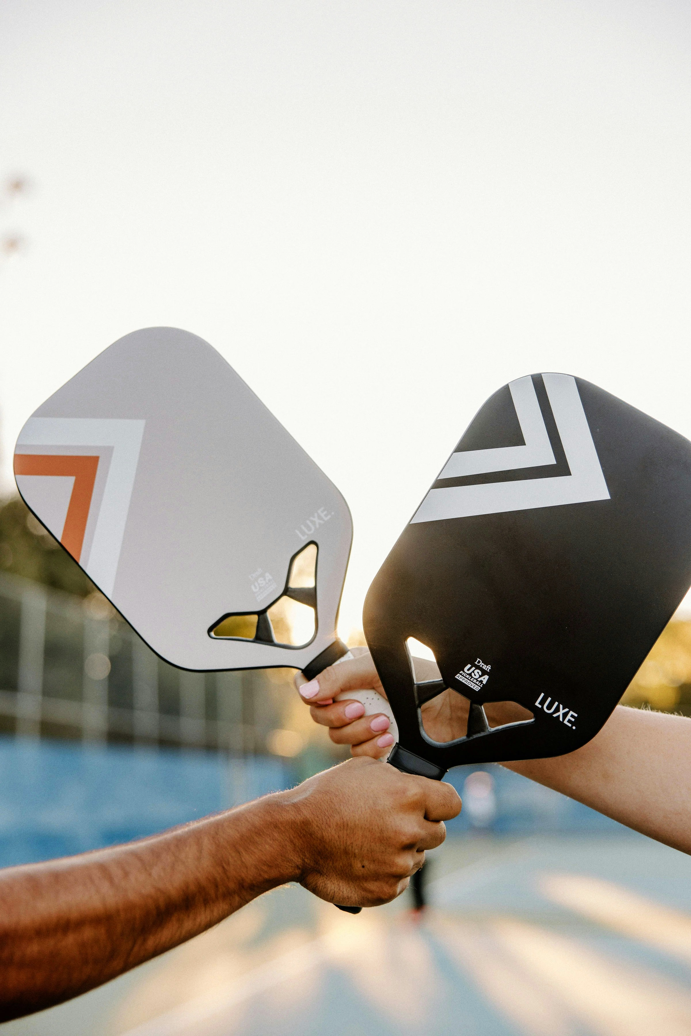 Two people holding paddle pickleball rackets, one with a white racket and one with a black racket, during a game outdoors, at Britton Park Apartment's pickleball court