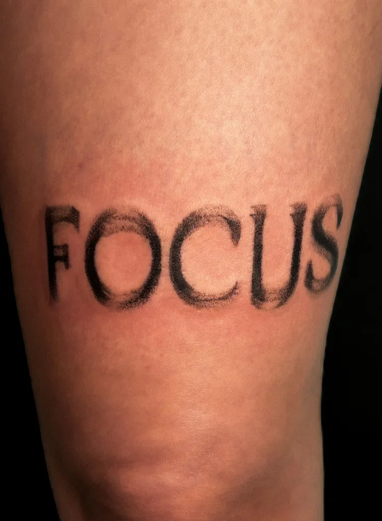 Tattoo of the word 'FOCUS' on skin with a distressed, faded style.
