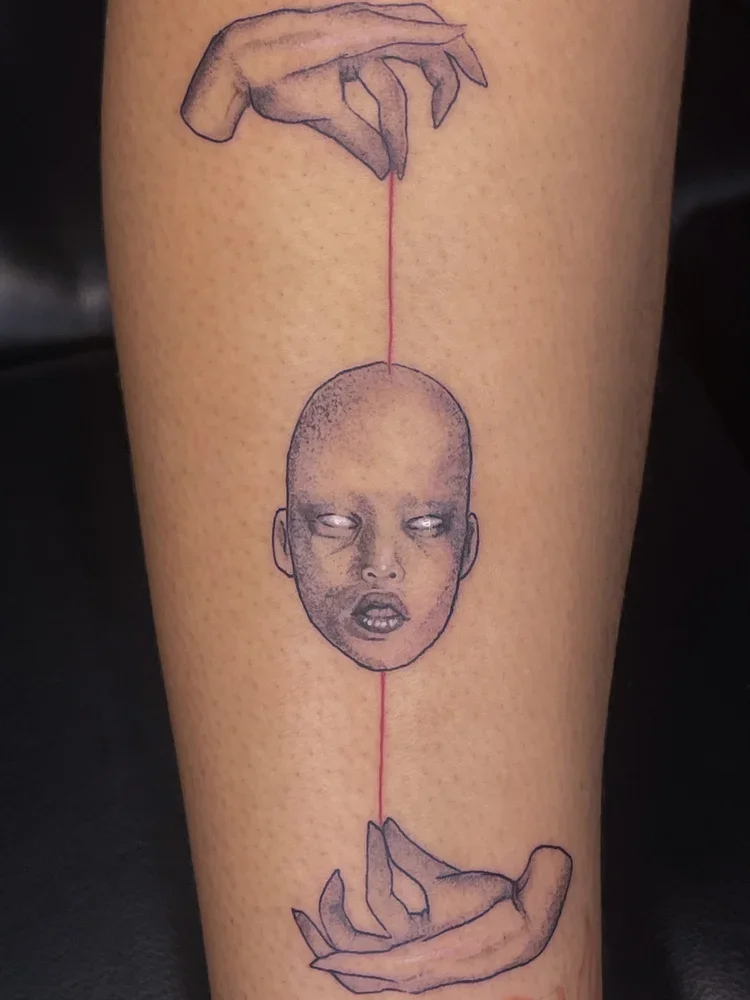 Tattoo of two hands holding a line with a child's face in the middle, with eyes closed and mouth slightly open.