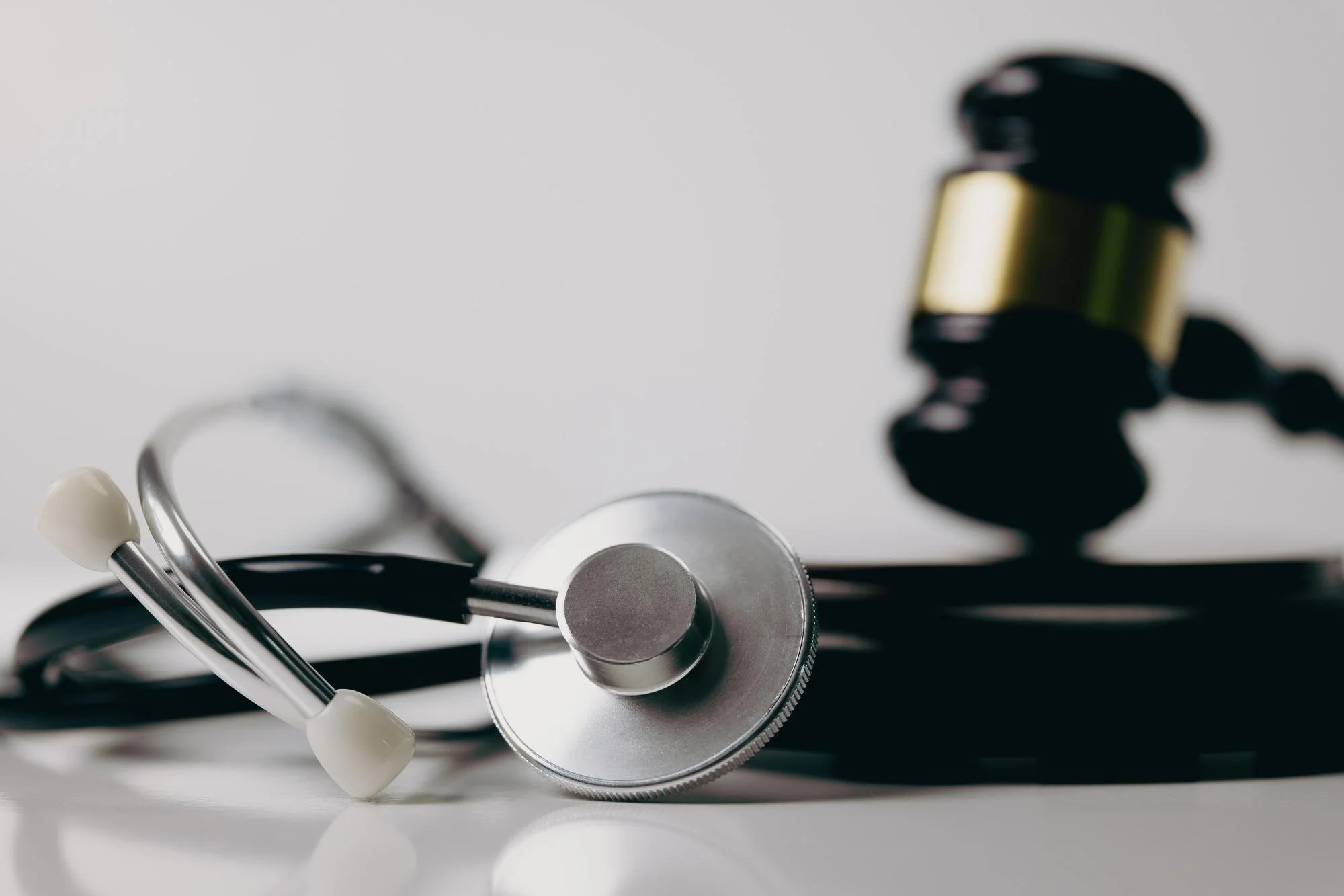 Close-up of medical instruments including a stethoscope and a tuning fork on a white surface with a blurred background.