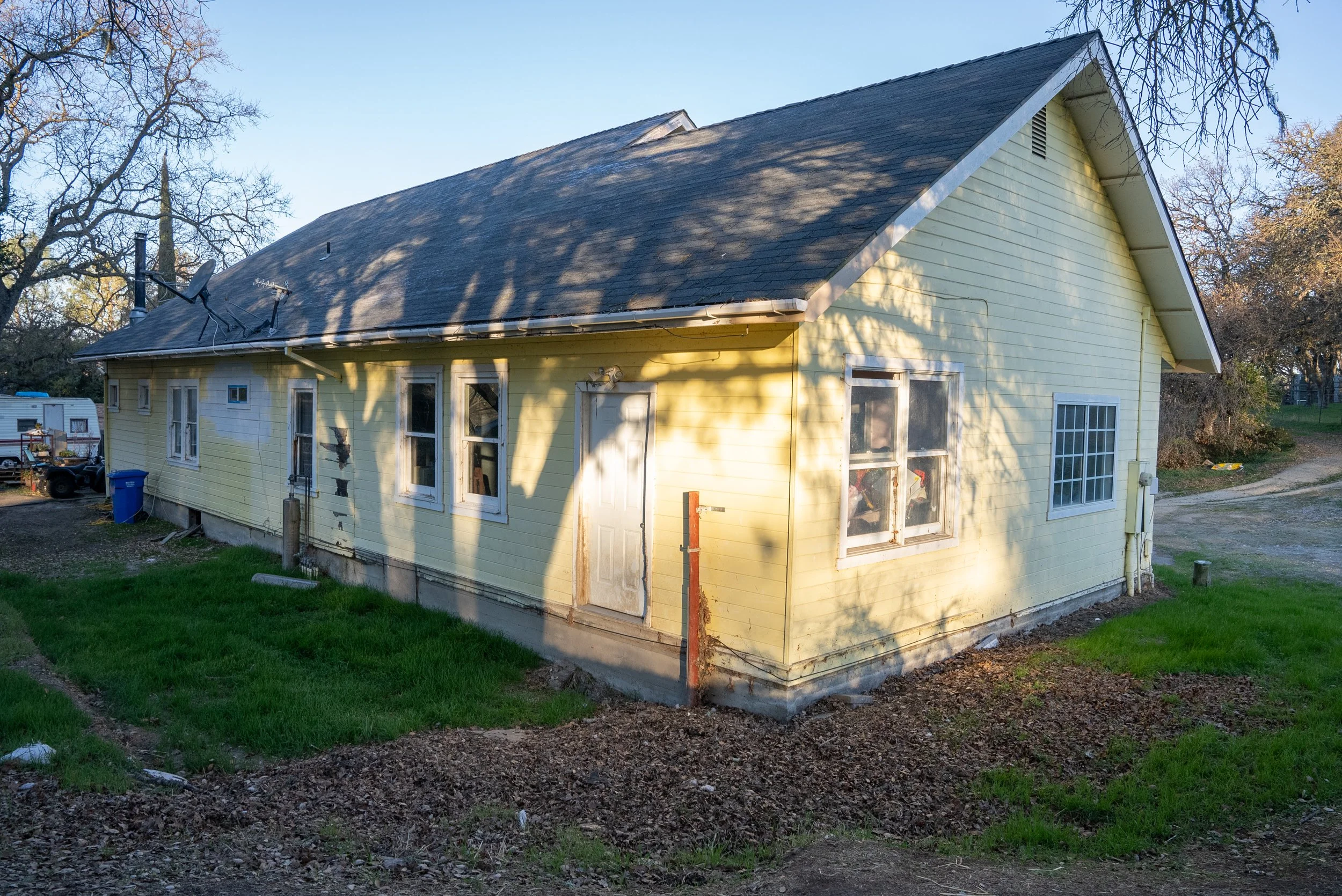Yellow house with a gabled roof and multiple windows, surrounded by trees and grass in the yard.
