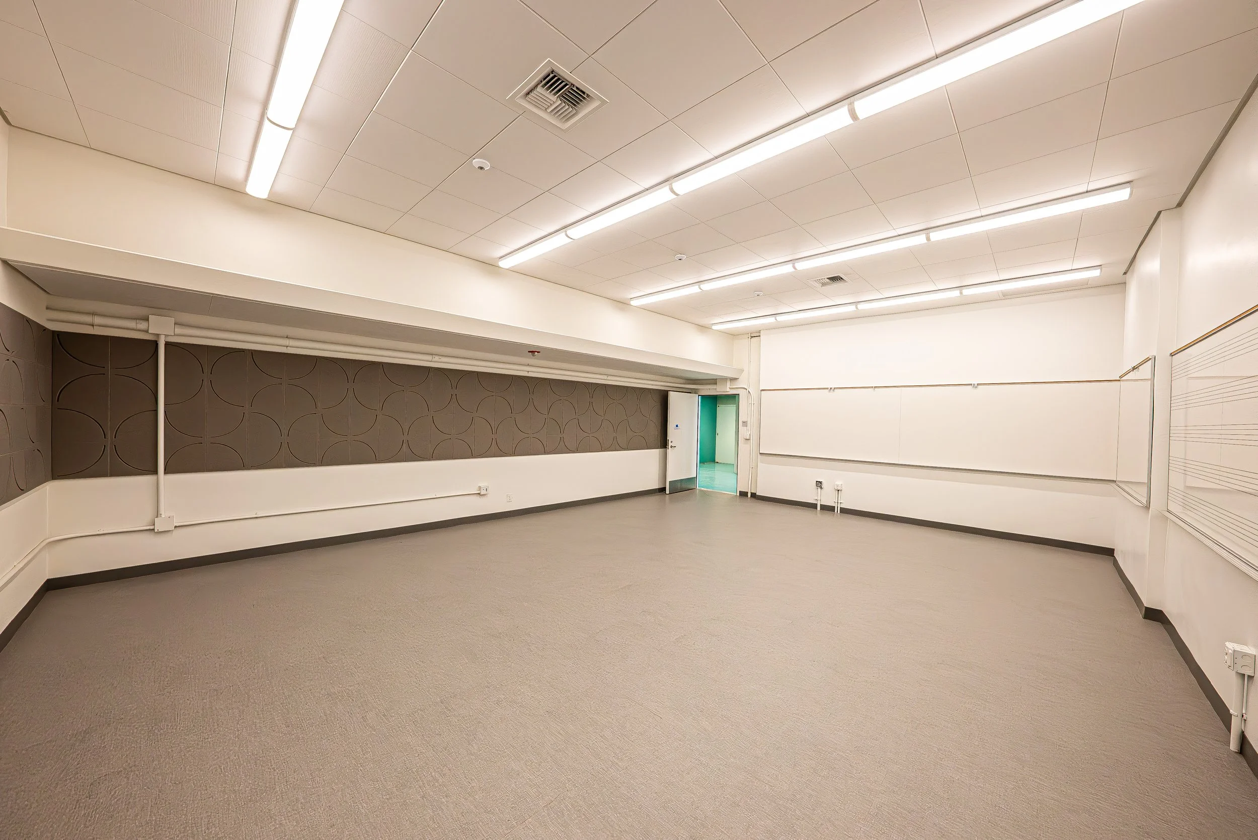 Empty beige room with ceiling lights, a door, and a wall with musical notes.