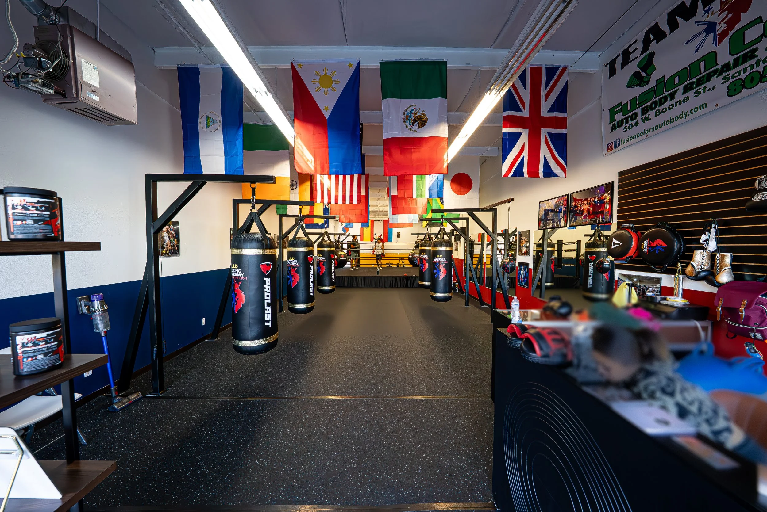 Inside a boxing gym with punching bags, boxing gloves, and flags from various countries hanging from the ceiling.