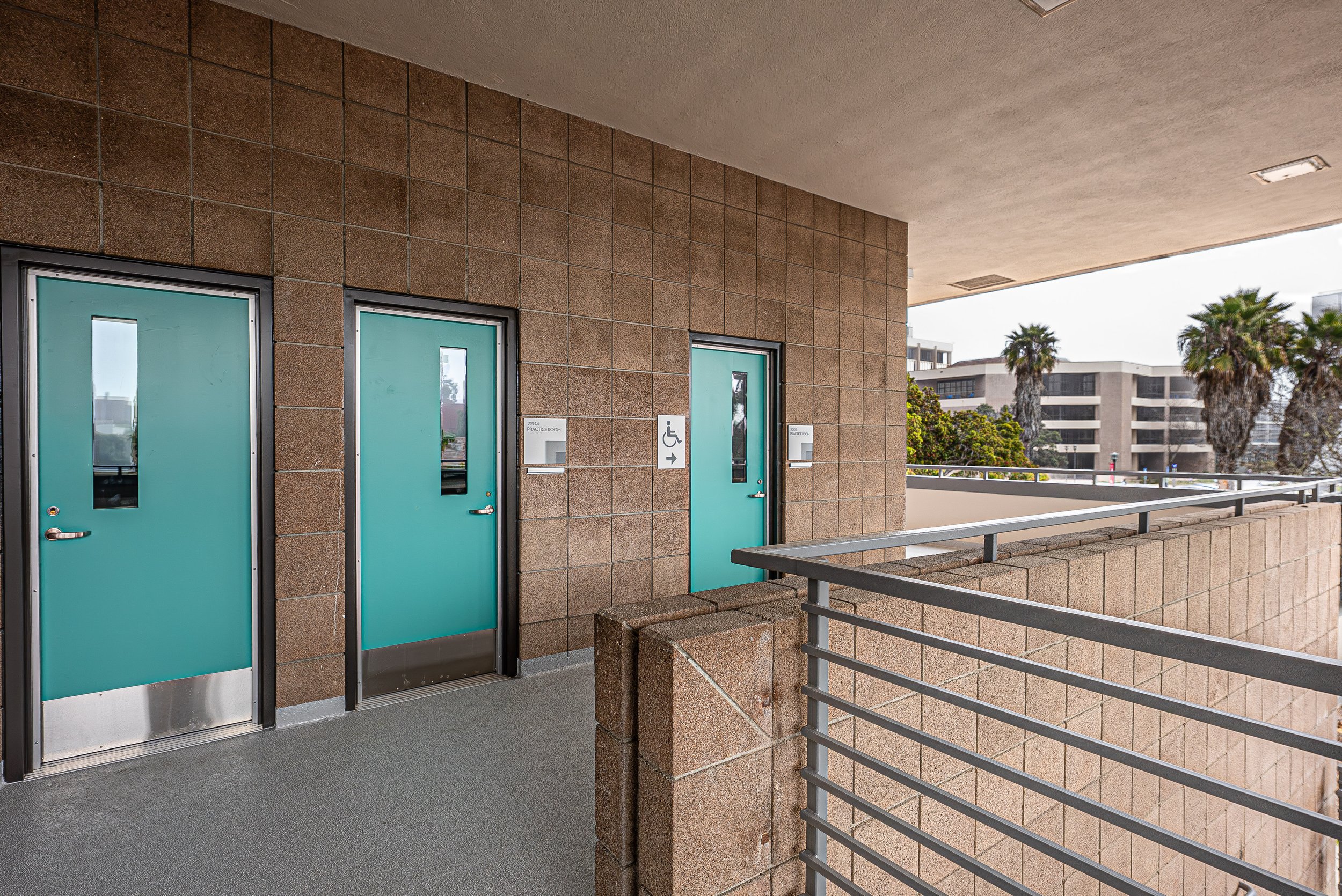Exterior of a building with turquoise doors, one with an accessible sign, a sign pointing right, and palm trees in the background.