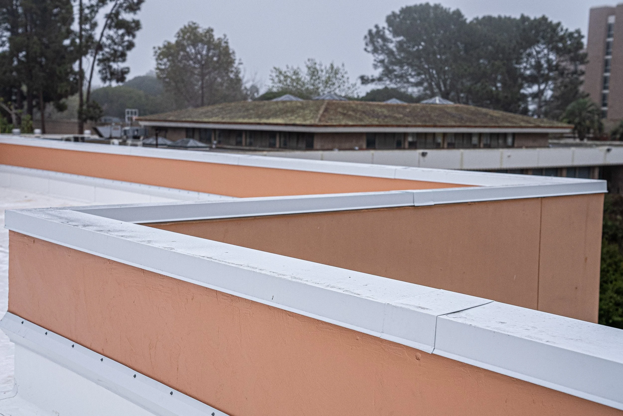 Multi-story building rooftop with a view of trees and a cloudy sky.
